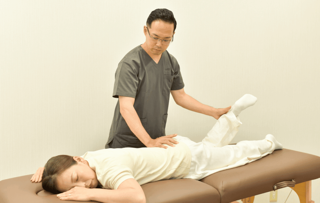 整骨院で生理前の腰痛ケアに通っている女性に対して施術者が骨盤調整をしている姿